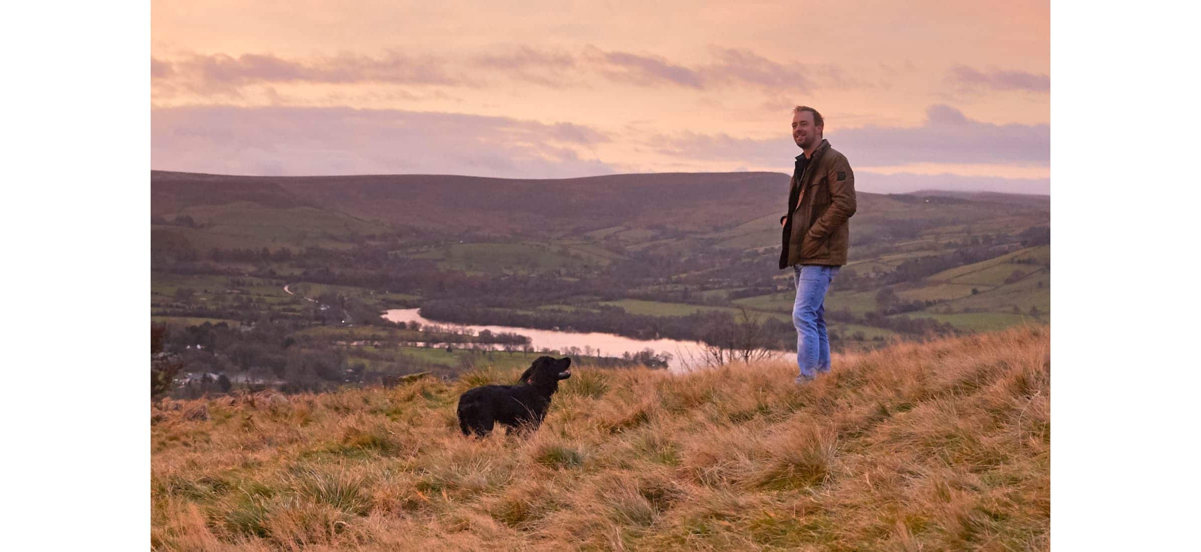 Dan Capper and his dog on a hill overlooking a river and valley.